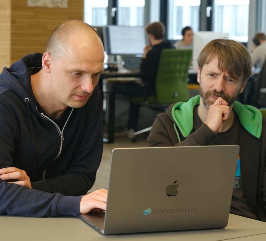 Zwei Personen sitzen an einem Laptop zusammen und denken intensiv nach