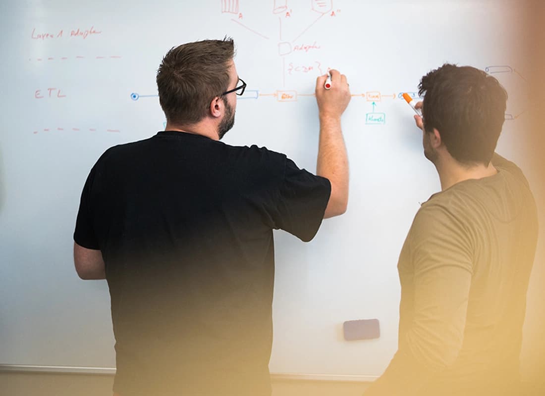 Zwei Personen stehen vor einem Whiteboard und zeichnen einen Prozess