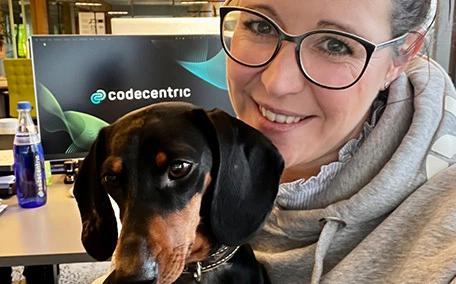 Eine Frau sitzt an einem Arbeitsplatz und macht zusammen mit einem Hund ein Selfie