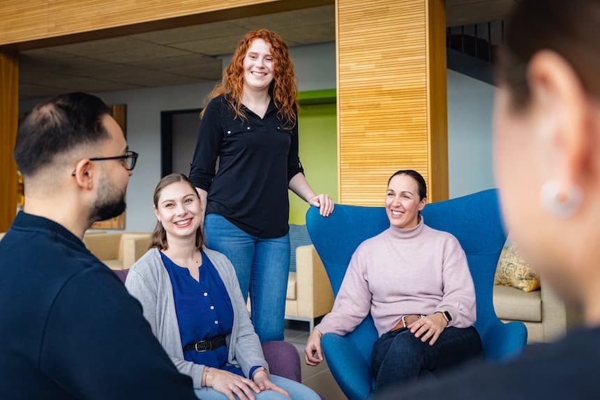 Eine Gruppe von Mitarbeitenden unterhält sich lächelnd in einer modernen Büro-Lounge.