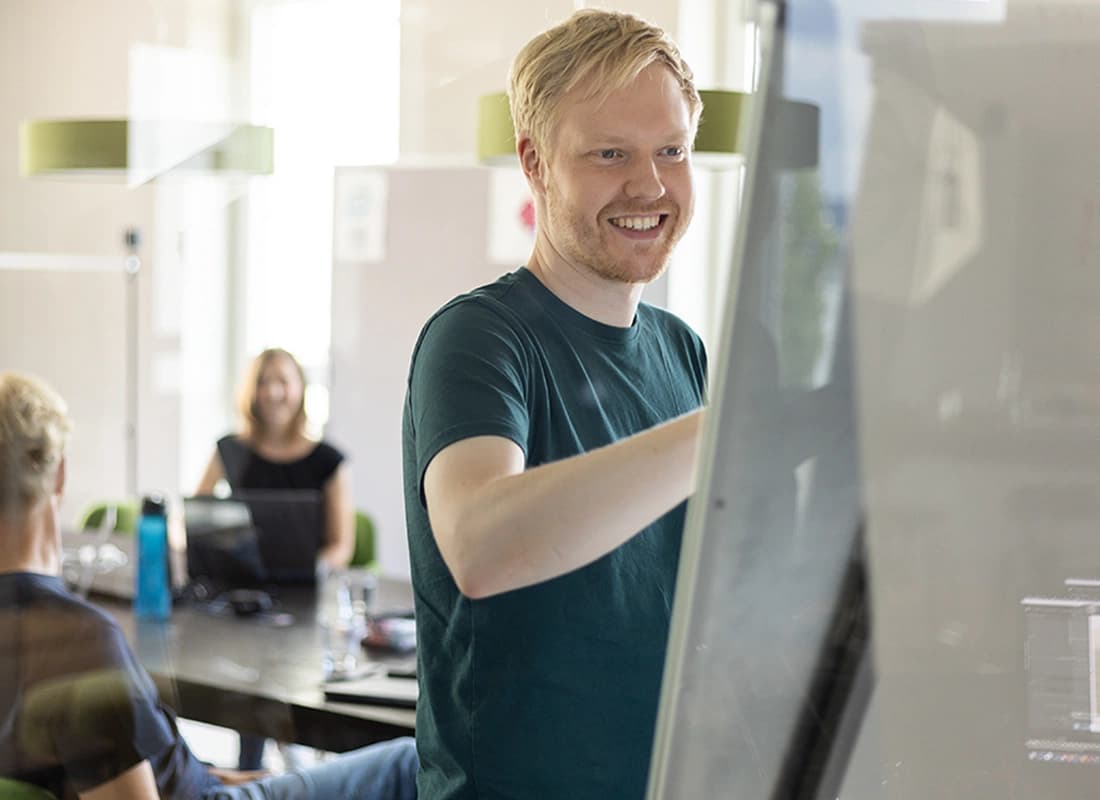 Mann steht am Flipchart, das nur von hinten zu sehen ist, dahinter sind Personen am Tisch