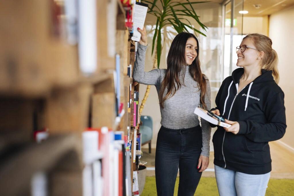 Jenny steht mit einer Kollegin an einem Bücherregal bei codecentric.