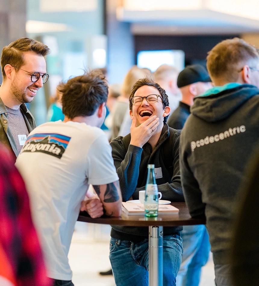 Vier Männer stehen um einen Stehtisch herum, unterhalten sich und lachen herzhaft